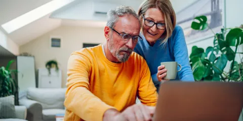Middle aged couple in living room looking at laptop 