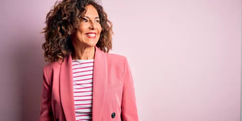 woman with brown curly hair and pink blazer, smiling 