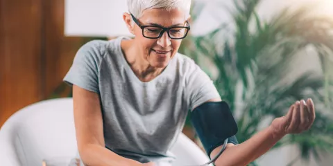 Senior woman with glasses and short grey hair, sitting and taking blood pressure