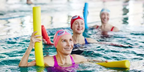 3 women in pool, smiling and using flotation noodles exercising 