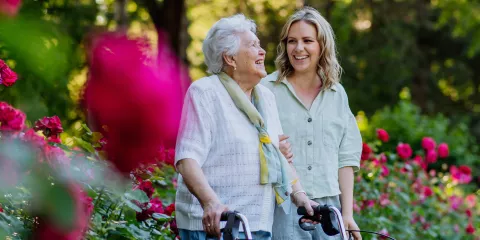 Senior woman smiling and walking with caregiver outside 