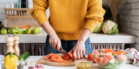 Woman in kitchen cutting tomatoes on cutting board, surrounded by vegetables 