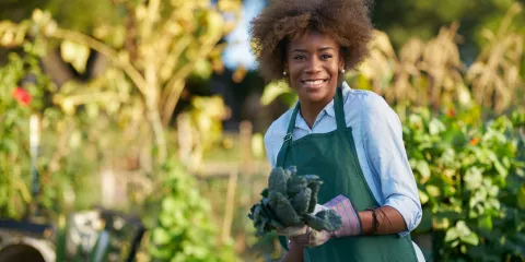 Woman in garden smiling with gardening gloves and holding a plant