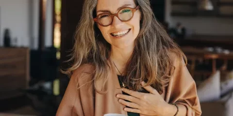 middle aged woman, hand over heart, smiling and holding coffee mug