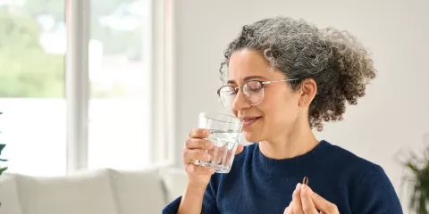 woman in blue shirt, taking pill with water 