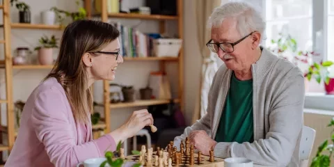 Caregiver smiling and playing chess with elderly man 