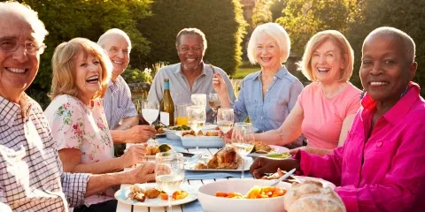 Seniors smiling and laughing at table with food outside
