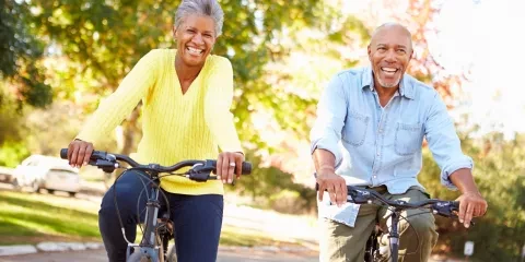Couple outside, riding bikes on path and smiling 