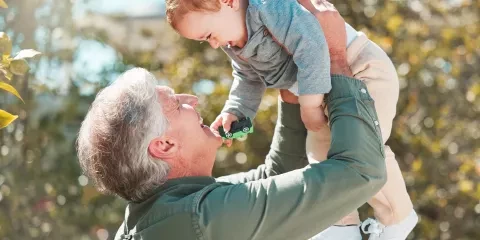 older man holding up his grandson and smiling 