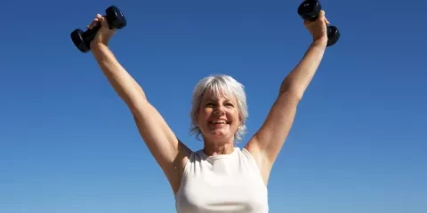 Woman outside holding weights above her head and smiling 