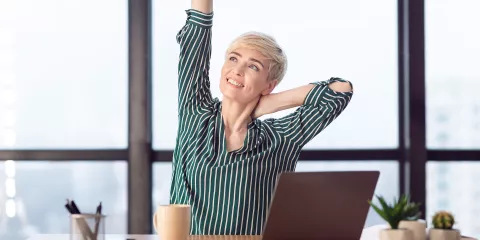 Woman in an office stretches her arms and neck while seated in her desk chair.