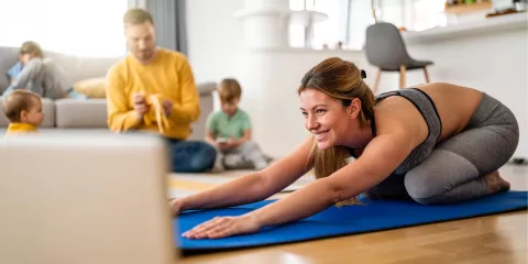Woman doing Yoga on mat in living room surrounded by husband and 2 kids