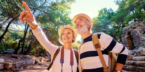 An older couple wearing hats and backpacks, the woman with a camera around her neck, enjoying nature while out on a hike.