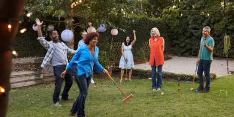 Couples laughing in backyard playing Croquet on lawn