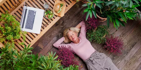 A woman has set her work laptop aside to take a break laying down on her wooden patio garden.