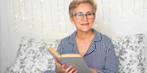 Older woman in pajamas on couch reading a book in the evening
