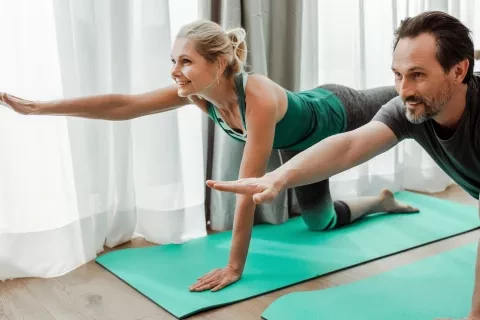 Middle-aged couple stretching out arms and legs on yoga mat indoors
