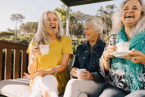 3 women enjoying tea and laughing on patio swing 