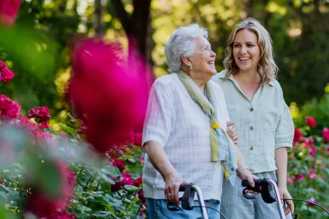 Senior woman smiling and walking with caregiver outside 