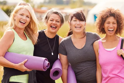 4 middle aged women, with workout clothes and yoga mats, smiling