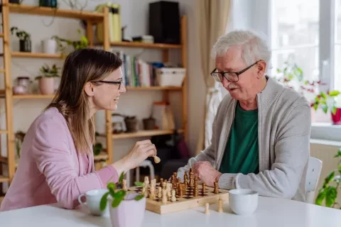 Caregiver smiling and playing chess with elderly man 