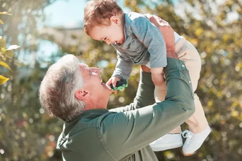 older man holding up his grandson and smiling 