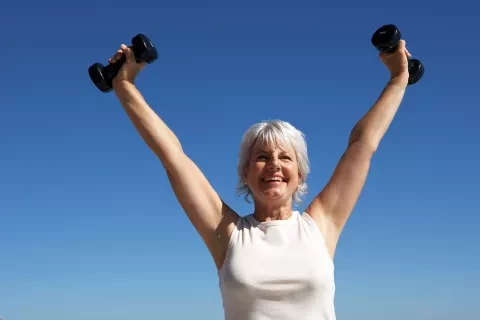 Woman outside holding weights above her head and smiling 
