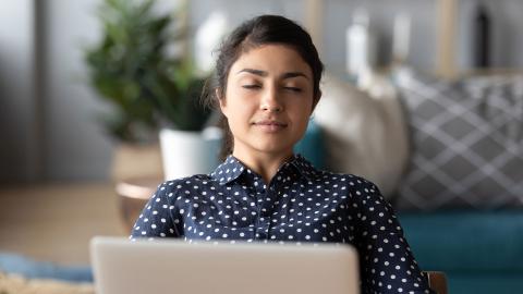 Woman seated at a laptop with eyes closed in meditative focus