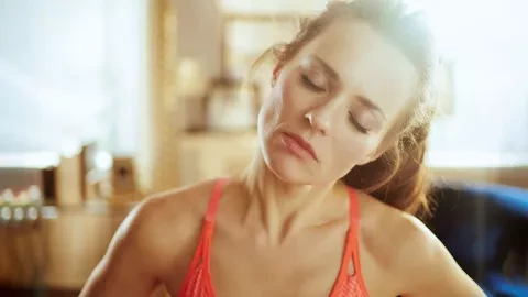 Woman in a sports top stretches her neck with eyes closed