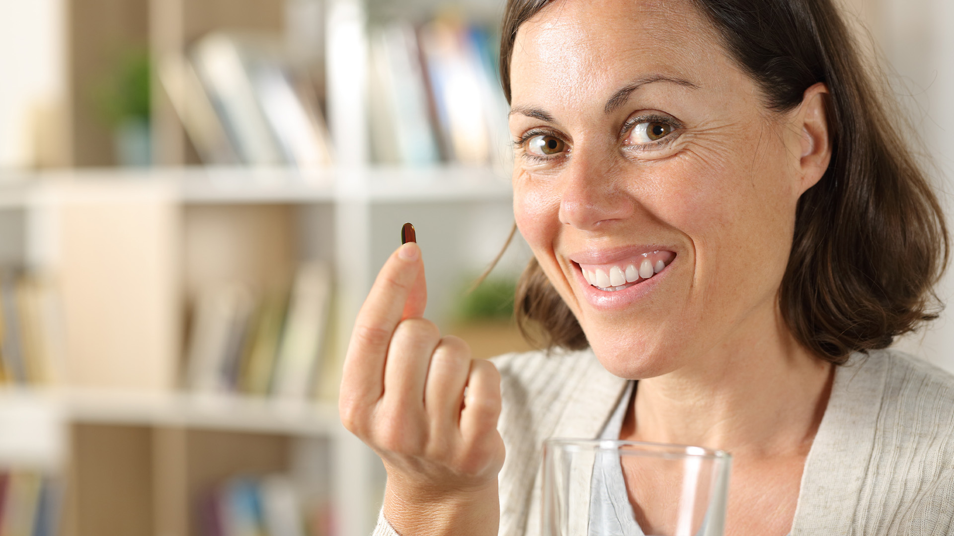 woman smiling and holding a supplement pill