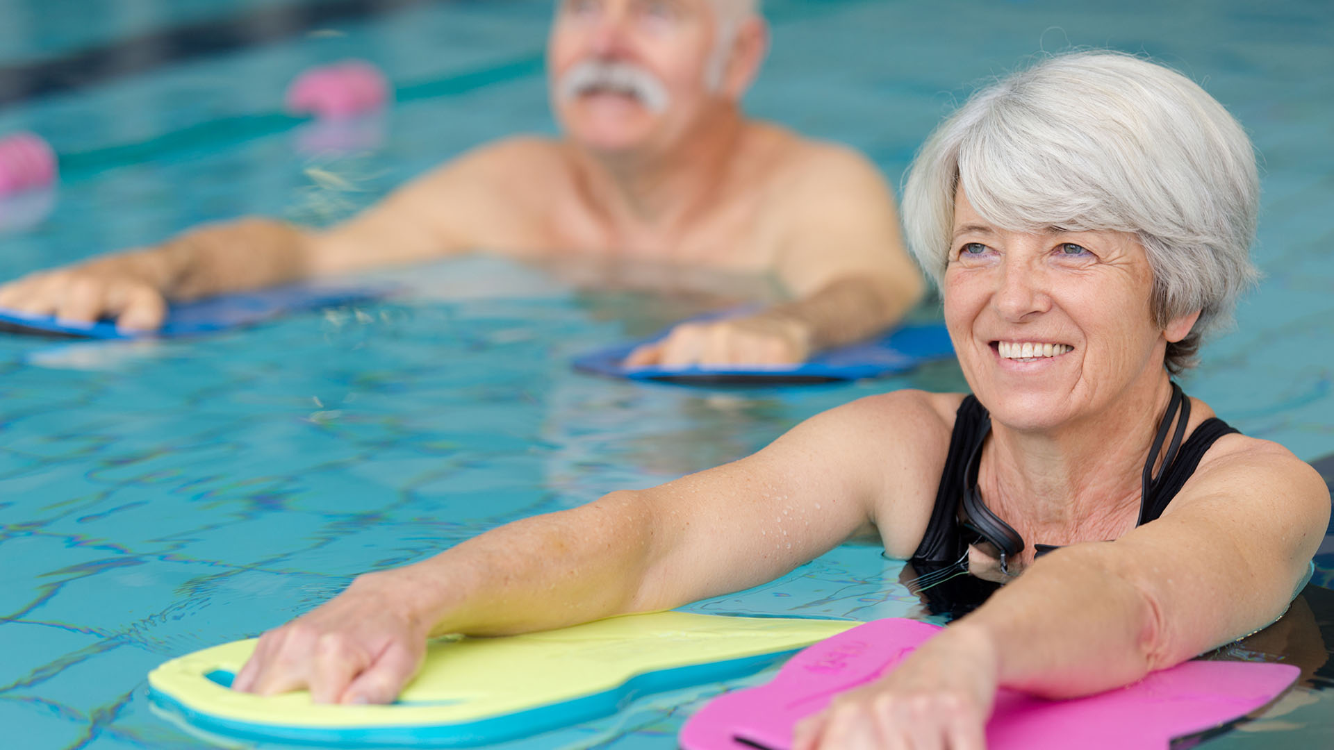 Older woman and man in pool with floats doing water aerobics and smiling