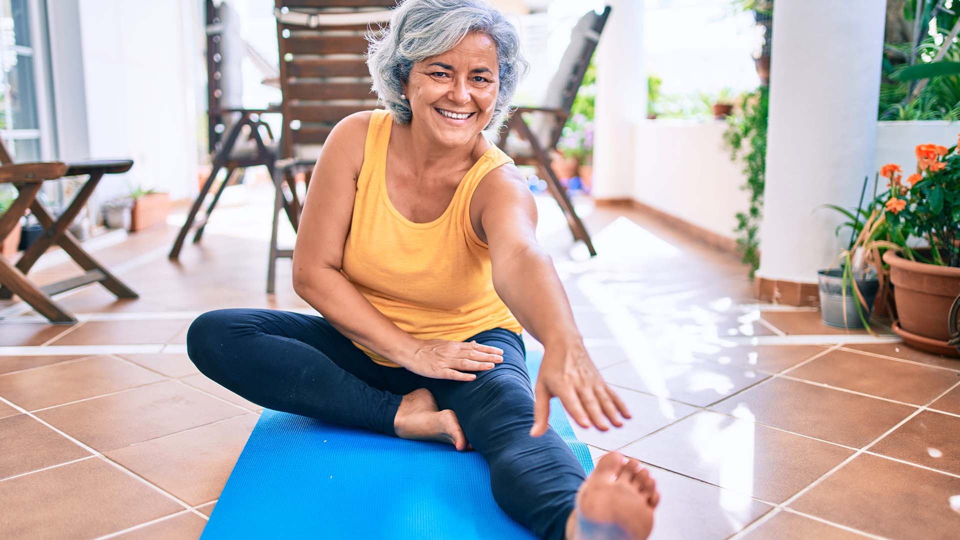 Older woman sitting on yoga mat, stretching arm to toe